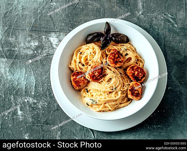 Zucchini Parmesan Meatballs with Pasta Carbonara in white plate over gray background. Close up view of creamy carbonara with copy space left