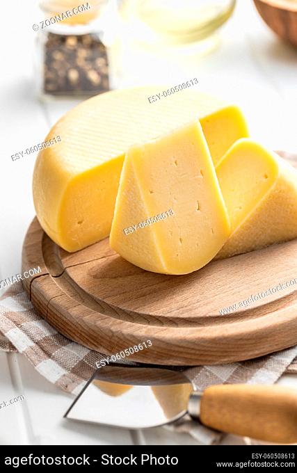 Block of hard cheese. Sliced cheese on cutting board
