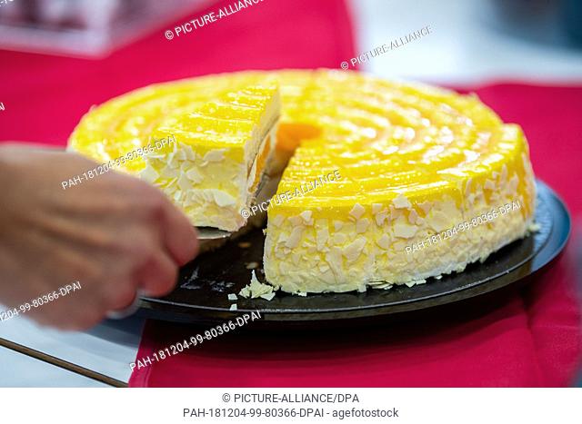 04 December 2018, North Rhine-Westphalia, Mettingen: A person lifts a piece of tangerine mascarpone cake from a plate by the food manufacturer Coppenrath and...