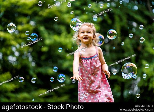 Happy girl enjoying while running amidst bubbles at park