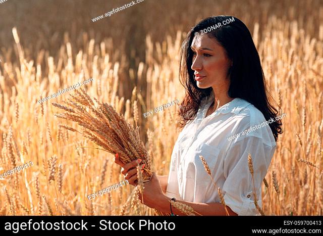 Young Woman edge lit portrait holding sheaf of wheat ears at agricultural field