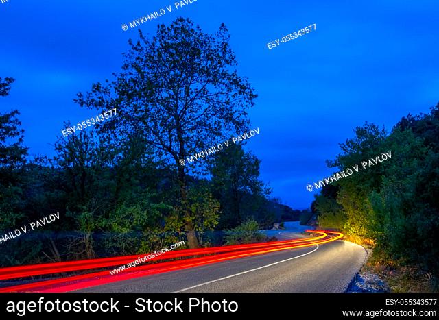 Tail lights illuminate an empty road in a night summer forest. Long winding trails