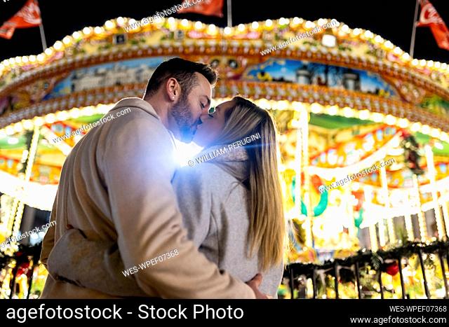 Couple kissing each other in front of carousel at Christmas market