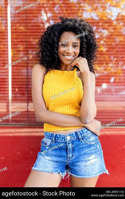 Smiling young woman standing in front of red window