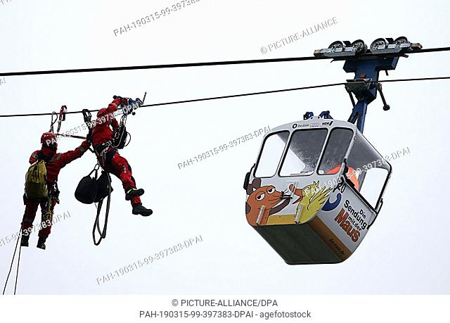 15 March 2019, North Rhine-Westphalia, Köln: During an exercise, fire brigade height rescuers approach the gondola of the cable car over the Rhine with a cable...