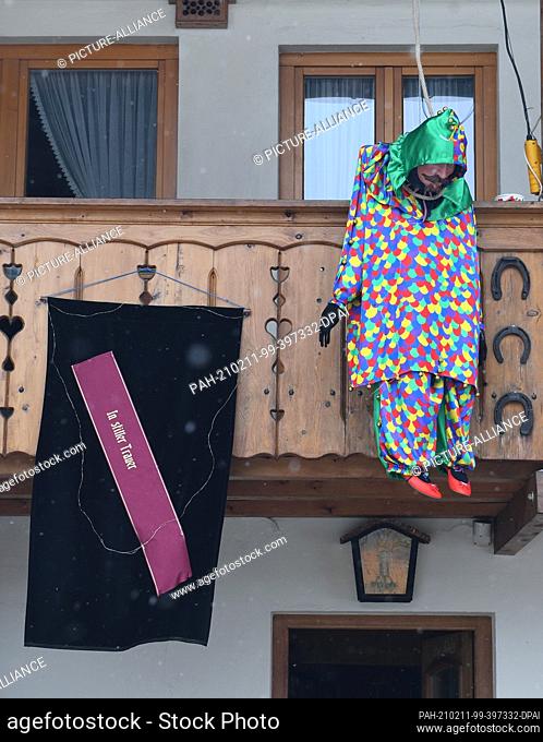11 February 2021, Bavaria, Farchant: ""In silent mourning"" can be seen on a grave sash next to a traditional carnival figure hanging from a gallows