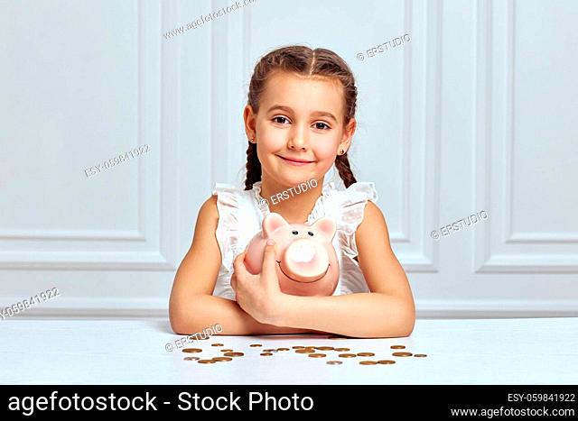 cute little child girl saving money for future in pink piggy bank. child hugs a piggy bank