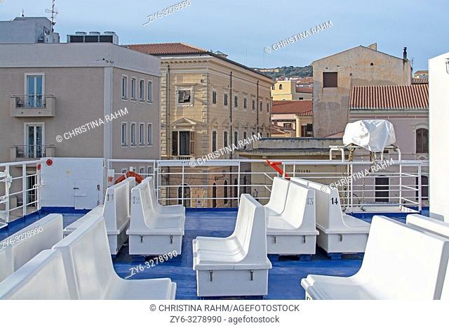ISOLA MADDALENA, SARDINIA, ITALY - MARCH 7, 2019: Ferry seats on sundeck and port area city view with sea promenade on a sunny afternoon on March 7