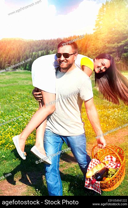 Smiling man holding girlfriend on his shoulder, couple are going to have a picnic