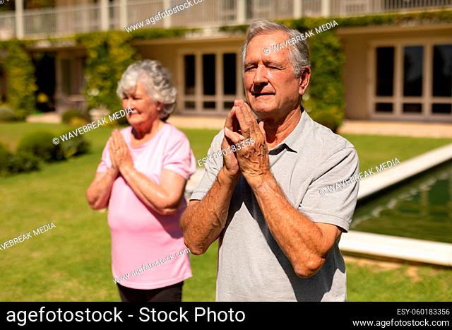 Senior caucasian couple practicing yoga, meditating in sunny garden