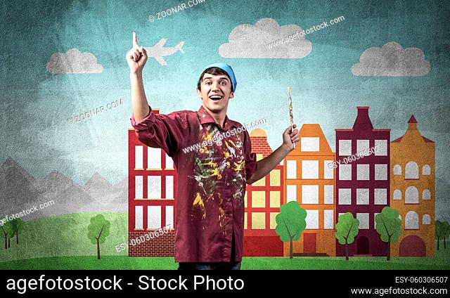 Young male artist holding paintbrush. Happy painter in shirt and bandana standing on background colorful picture on wall