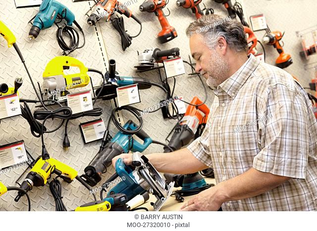 Side view of mature salesperson looking at electric saw