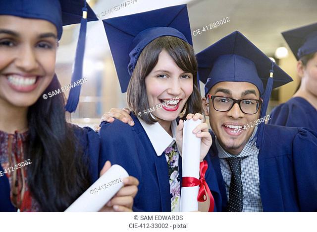 Portrait enthusiastic college graduates in cap and gown posing with diploma