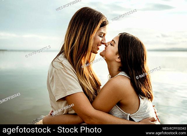 Mother and daughter nuzzling nose by lake against sky