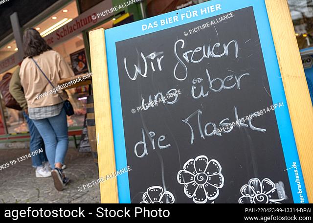23 April 2022, Bavaria, Munich: A sign reading ""We're happy about the mask"" stands in front of a store on the Viktualienmarkt