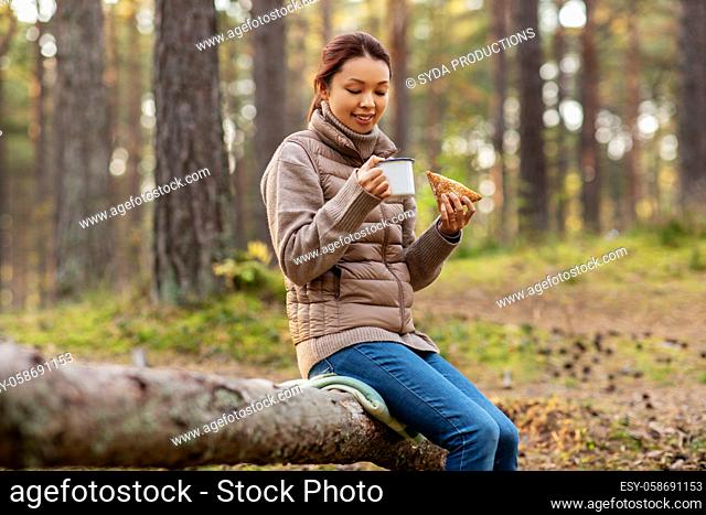 woman drinking tea and eating sandwich in forest