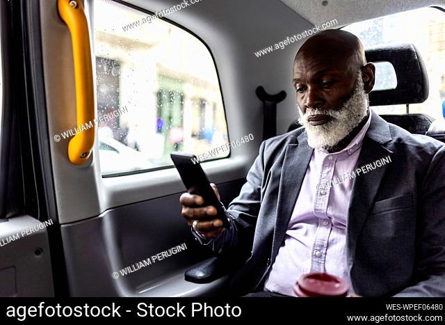 Senior passenger using mobile phone in back seat of taxi