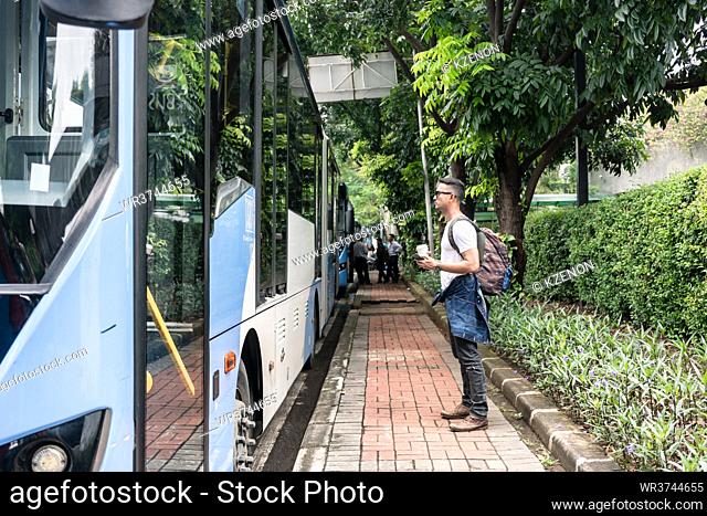 Full length side view of a young male tourist waiting for the bus in the station for public transport in Jakarta