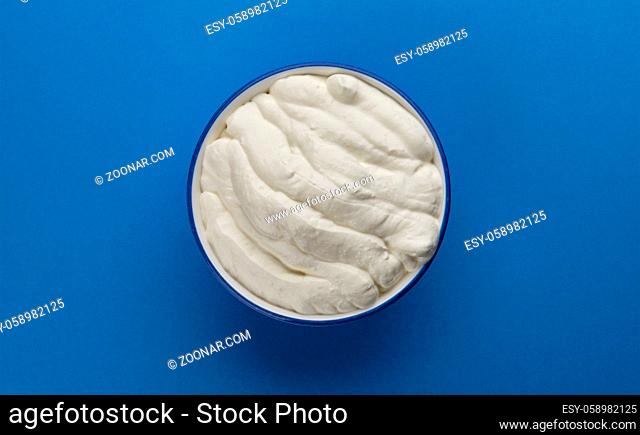 Bowl of sour cream on blue background, top view