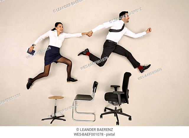 Businessman jumping with his female colleague over chairs