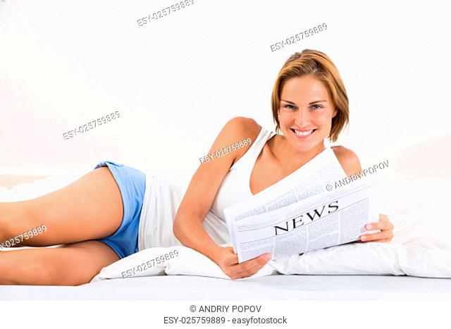Young Happy Woman Lying In Bed With Newspaper