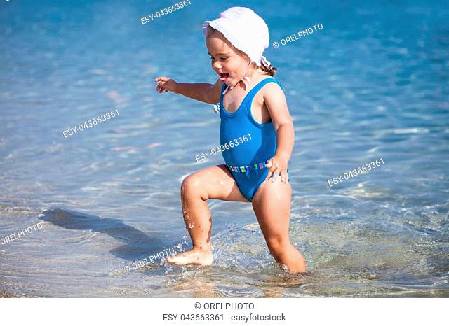 Little child girl is playing on sandy beach near blue sea
