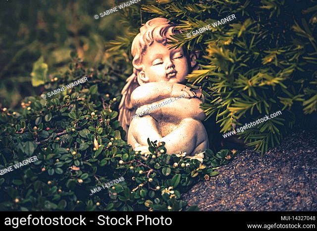 A sleeping angel sits with folded arms on a grave between trees