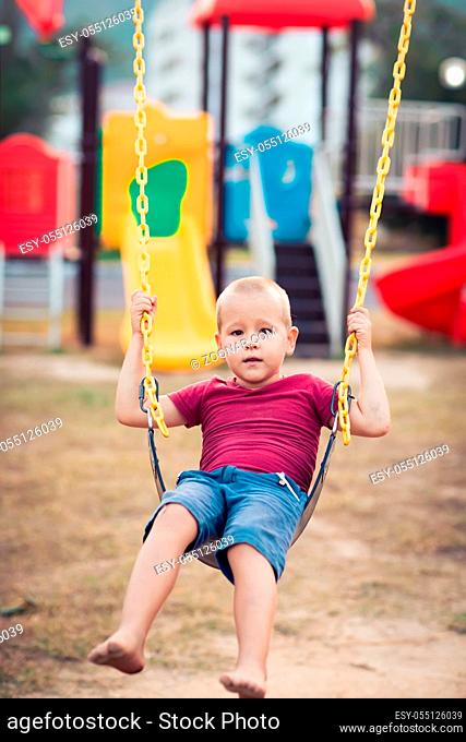 Little boy swinging on a swing at kids playground outdoor