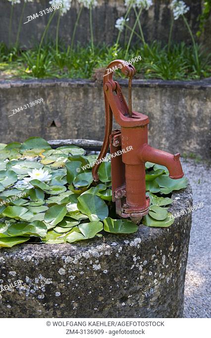 A well with a red hand pump and water lilies in the garden at La Bastide de Moustiers, a house converted to a hotel, in Moustiers-Sainte-Marie