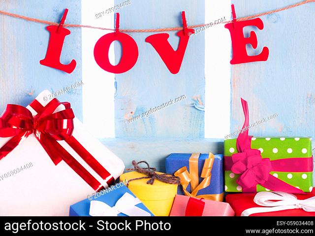 Love written from red paper letters and tied to a string with wooden clips, on a blue wooden fence and an abundance of multicolor gift boxes