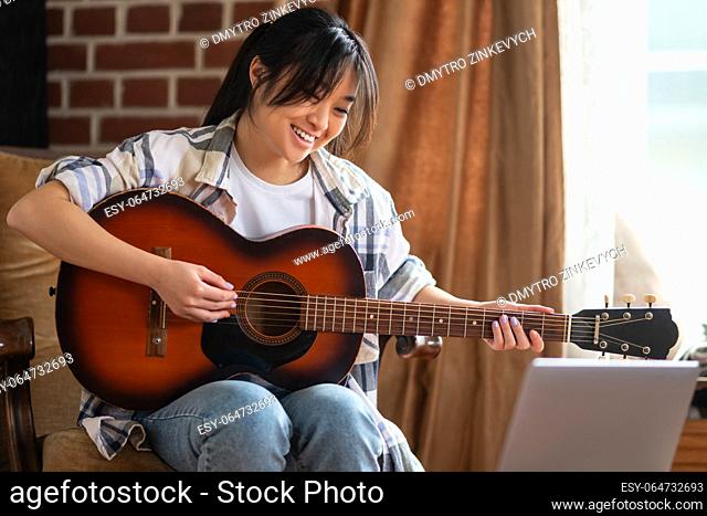 Playing guitar. Young asian girl playing the guitar at home