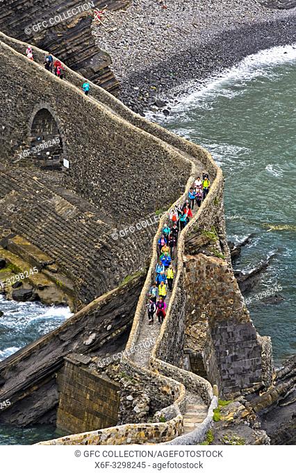 Visitors crossing teh stone bridge to the islet Gaztelugatxe near Bakio, Costa Vasca, Bay of Biscay, Basque Country, Spanien