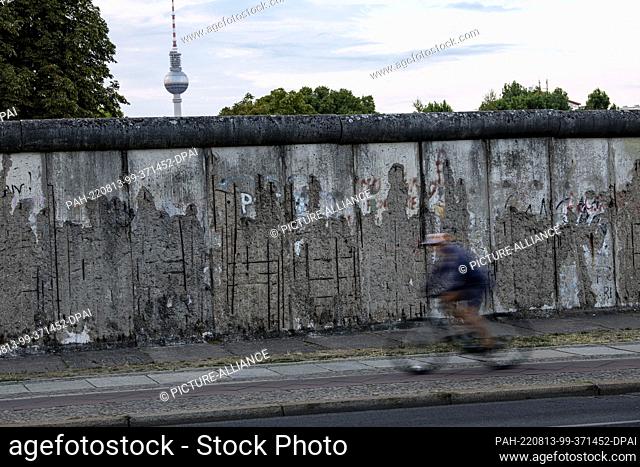 13 August 2022, Berlin: A cyclist rides past the Berlin Wall memorial early in the morning. The GDR had begun building the Wall around the western part of...