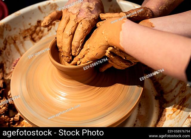Expert potter teach a child to work on potter wheel. Closeup of dirty hands