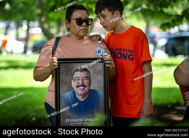 Nubia Hogan, left and her son Brian Hogan, 13, stand in the shade of a tree, with a photo of her father Eduardo Uvaldo, who was killed in the recent mass...
