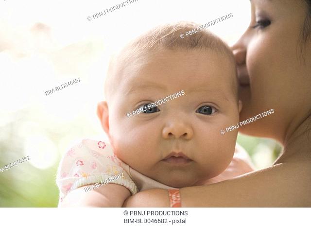 Hispanic baby looking over mother’s shoulder