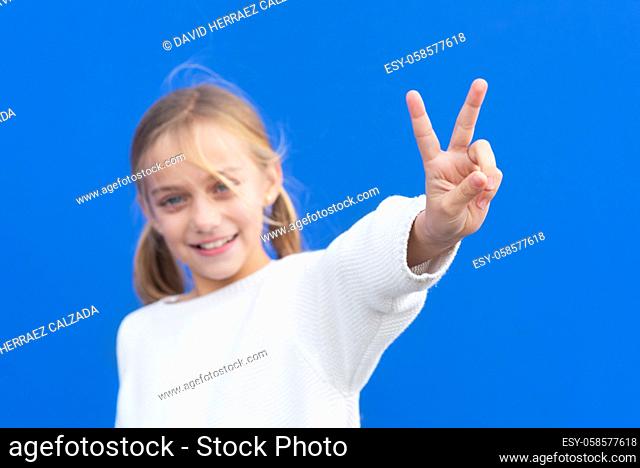 Young beautiful blond girl wearing casual sweater over blue background smiling looking to the camera showing fingers doing victory sign. number two