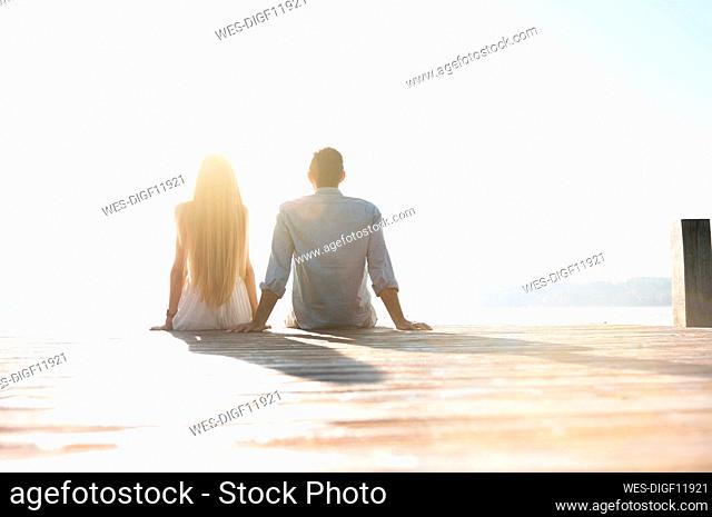 Back view of young couple relaxing side by side on jetty