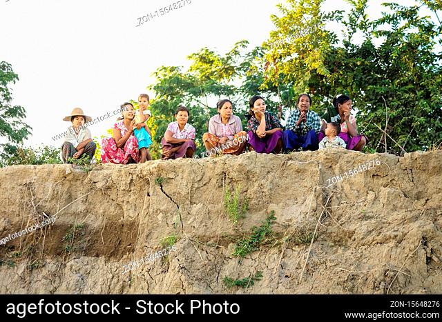 Irrawaddy river, Myanmar - December 26 2012: Women sitting, crouching and watching on a riverbank in a village along
