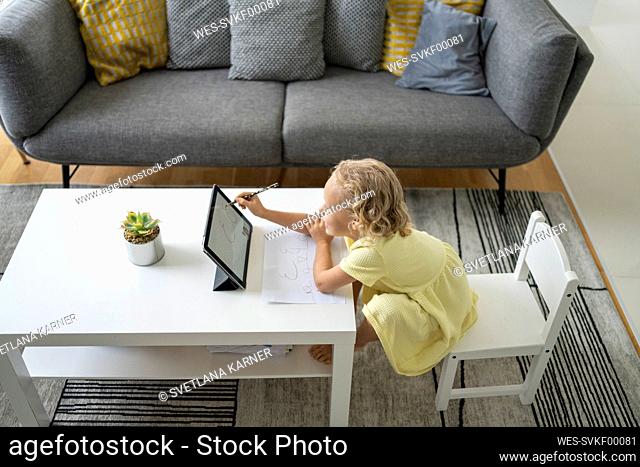 Girl with pencil using tablet PC sitting on chair at home