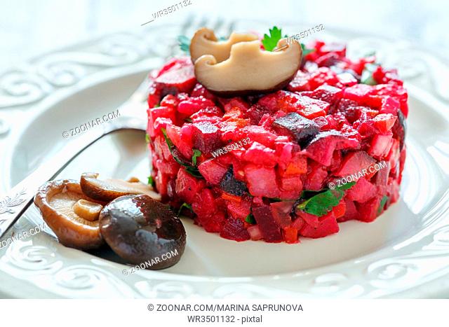 Russian salad with marinated mushrooms on a white plate closeup selective focus
