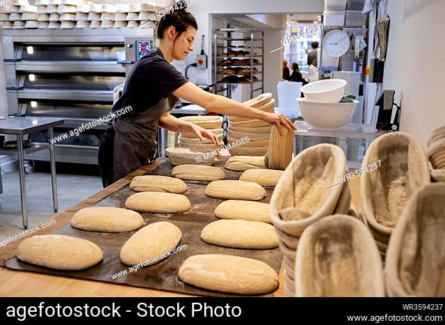 Woman wearing apron standing in an artisan bakery, shaping sourdough loaves for baking