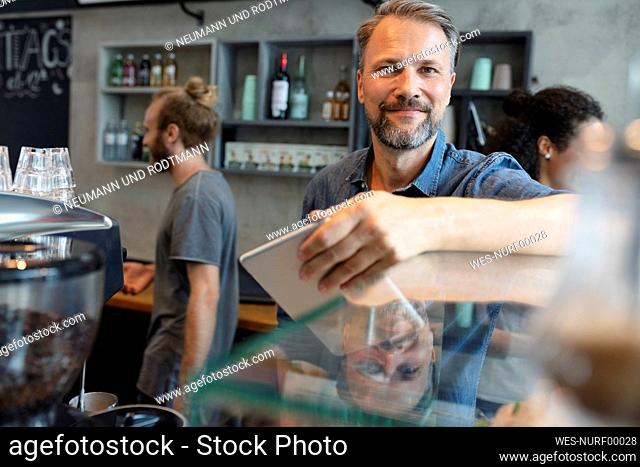 Smiling coffee shop owner standing behind cabinet in cafe
