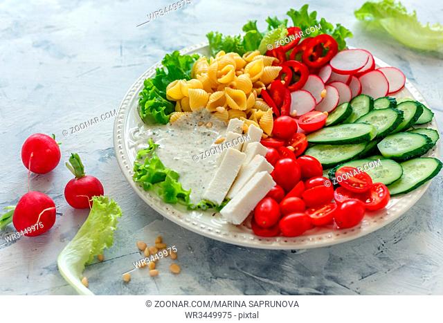 Dish with salad of fresh vegetables, pasta and artisan cheese on white table, selective focus