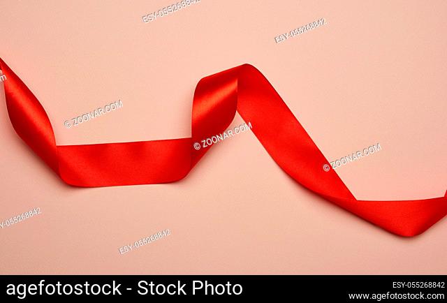 twisted red silk ribbon on a beige background, designer element for gift decor, close up