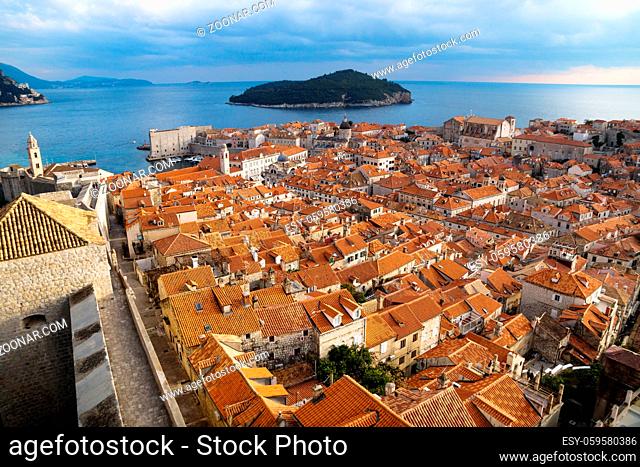 Panorama view of the mediterranean old town of Dubrovnik with orange tiled roofs, walkway on the fortress wall and view on ocean and island Lokrum, Croatia