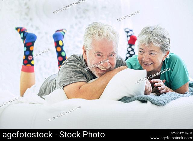 Senior couple lying on front and smiling on bed. Elderly couple spending leisure with each other lying on comfortable bed at modern house