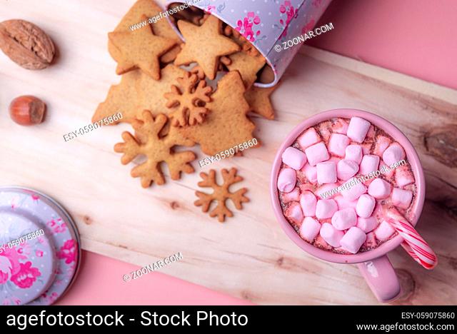 Christmas sweets context with a cup of hot cocoa with pink mini marshmallows, an overturned box with gingerbread cookies on a wooden platter