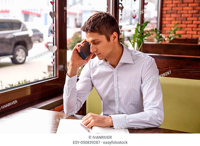 Young businessman in a suit working and talking on the phone. The manager works during coffee breaks. A man is sitting in a cafe