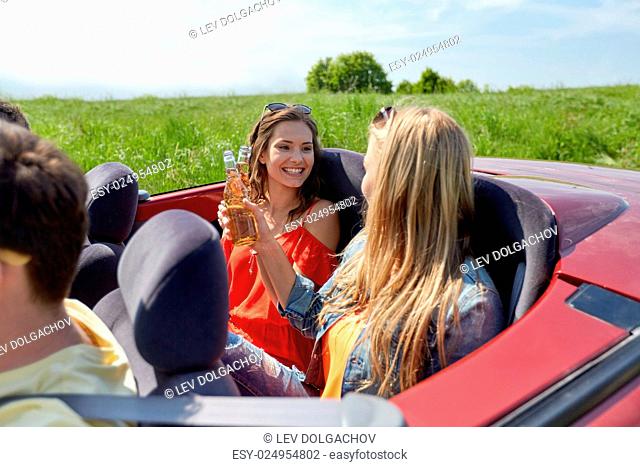 leisure, road trip, travel, summer holidays and people concept - happy friends driving in cabriolet car along country road and drinking beer